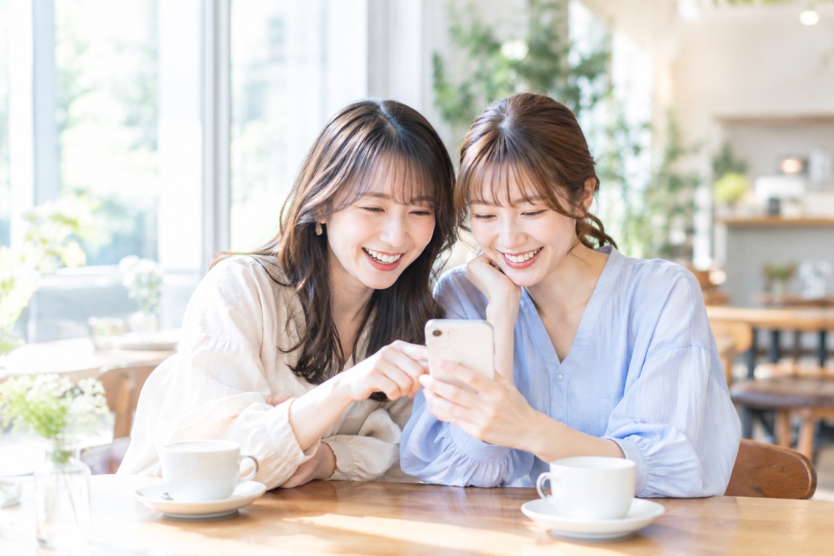 カフェでスマートフォンを一緒に見て笑う2人の女性